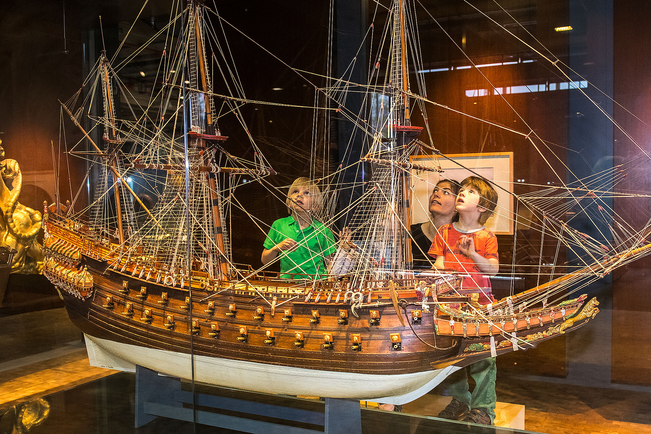Eine Frau und drei Kinder stehen vor einer Vitrine mit einem etwa drei Meter breiten und zwei Meter hohen Modell eines dreimastigen Segelschiffs. Das Modell besteht aus Holz, der Bauch des Schiffs ist weiß lackiert.