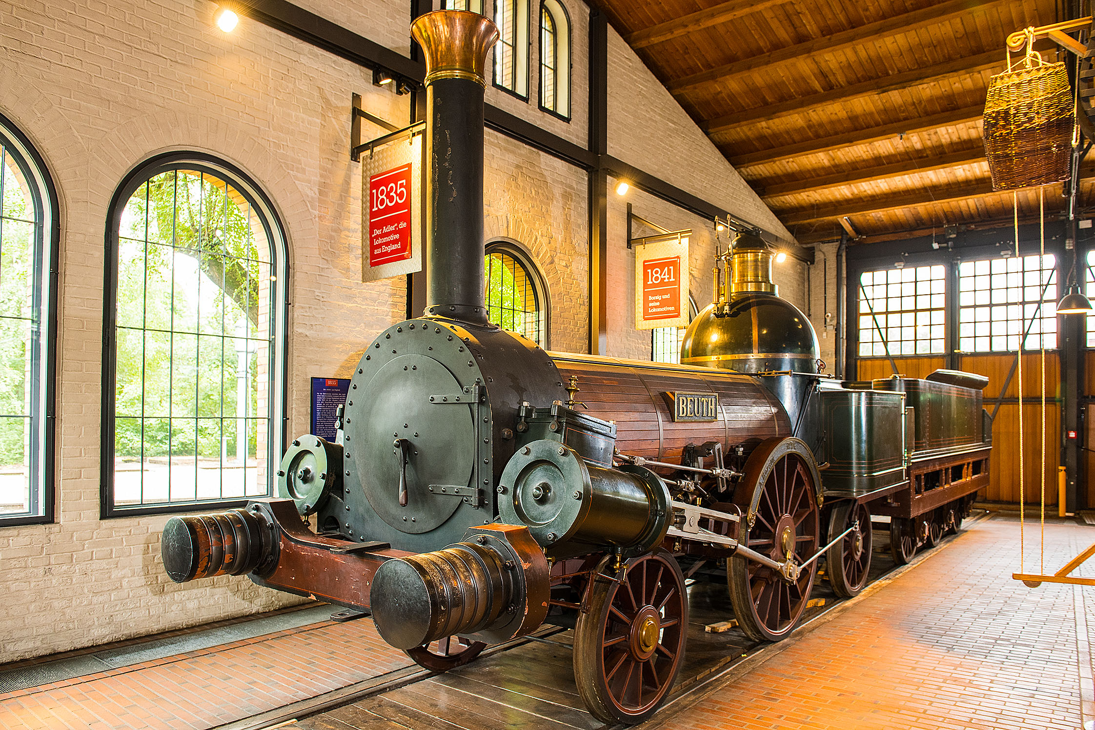 Eine Dampflokomotive aus Eisen, teilweise mit Holz verkleidet. Am hohen Schornstein und am Heizkessel befinden sind goldene Verzierungen. An der Seite ist der Schriftzug „Beuth“ angebracht.