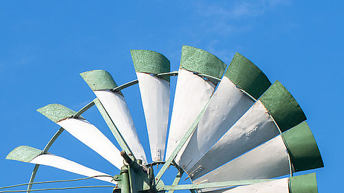 Weiß-grüne Flügelblätter eines Windrads vor blauem Himmel.