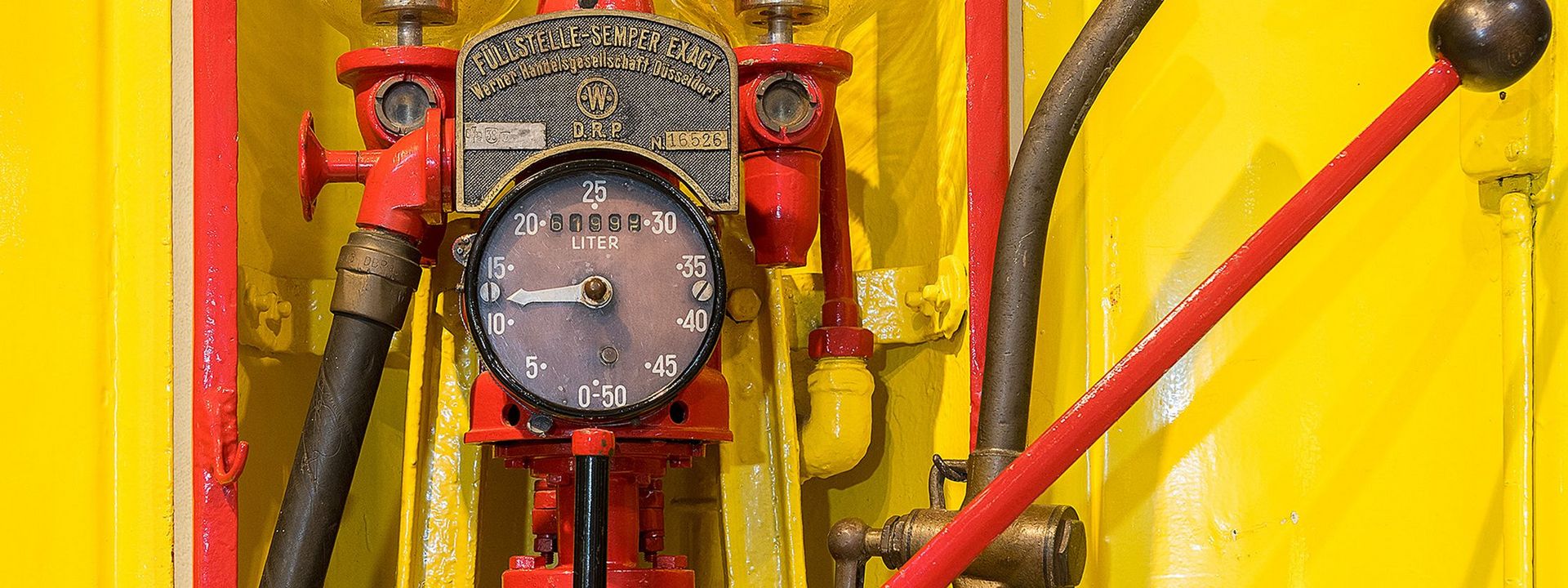 A yellow and red fuel pump. The arrow on the analog gauge in the middle points to between ten and 15. On the metal plate above it, the words “Füllstelle-Sempler Exact” (“Precision Sempler Fuel Pump”) are written.