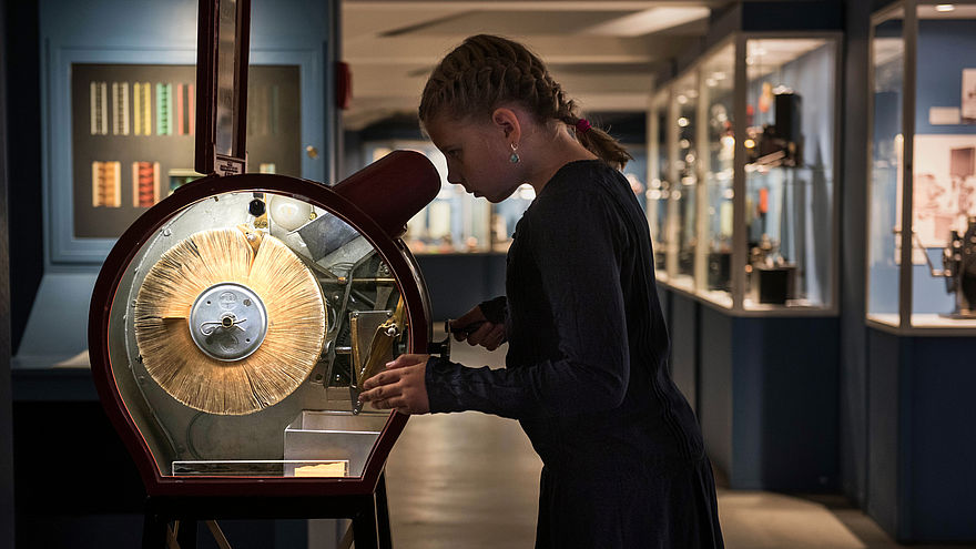 A girl looks into an illuminated case and turns a crank. Display cases with exhibits are in the background.