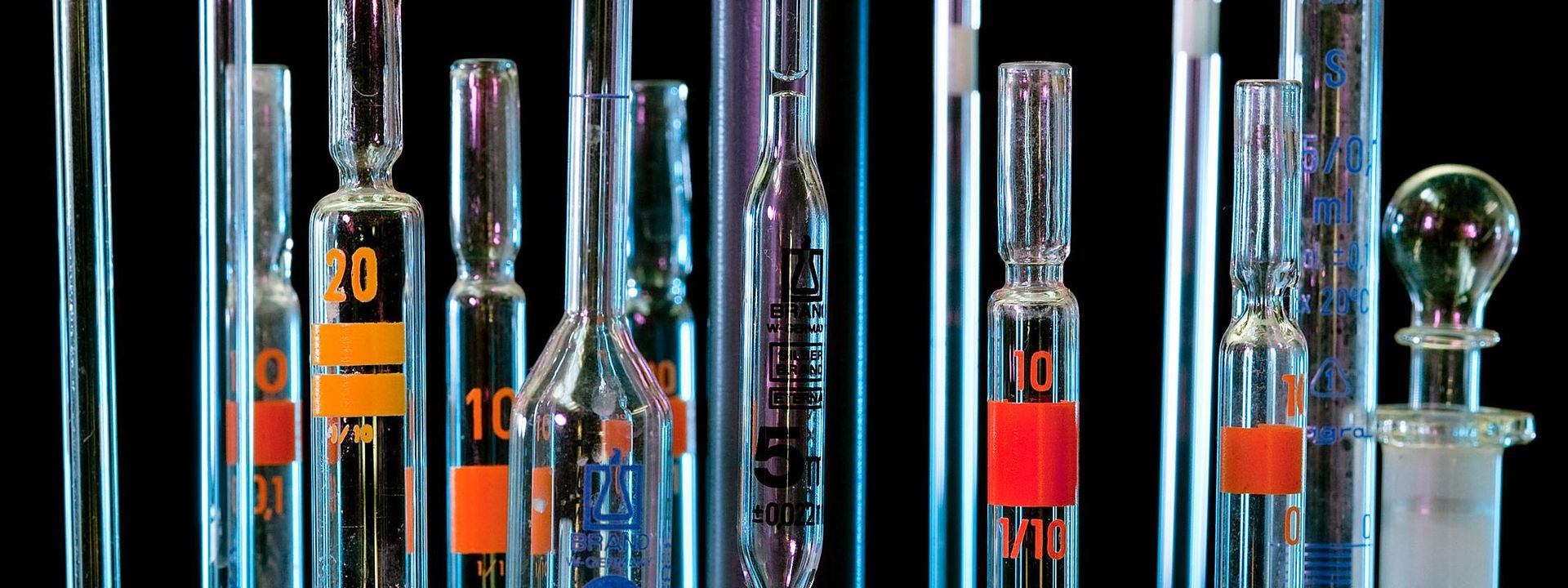 An ensemble of glass pipette tips in front of a black background.