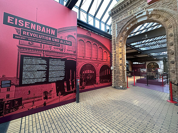 Blick in die überarbeitete Dauerausstellung Schienenverkehr. Links eine farbige Texttafel, rechts ist der historische Lokschuppen zu sehen.