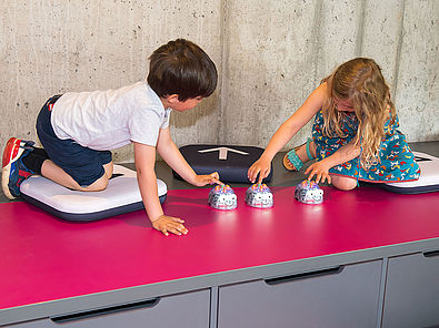 Zwei Kinder drücken die Startknöpfe mehrerer Robotik-Spielzeuge, die wie gläserne Mäuse aussehen.