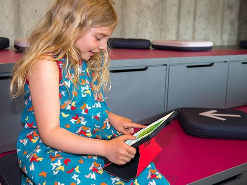 Ein Mädchen sitzt im farbenfrohen kids.digilab und sieht sich etwas auf einem iPad an.