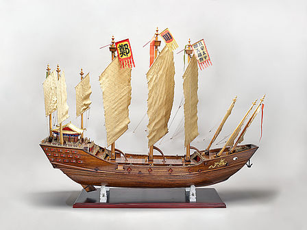 Das Schiffsmodell aus Holz steht auf einem kleinen Sockel und hat insgesamt 9 Masten mit Segeln und Fahnen.
