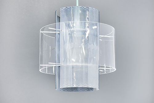 Die Lampe hängt an einem weißen Kabel. Die Glühbirne ist von durchsichtigen, rund gebogenen Plexiglasscheiben umschlossen, die mit eingravierten Zickzacklinien verziert sind.