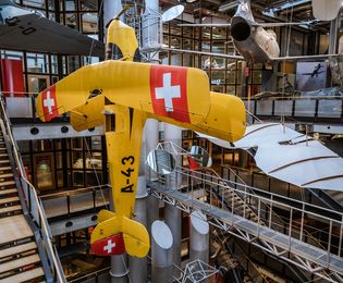 A large yellow airplane hangs nose-up in the atrium of the New Building. There are other airplanes and gliders hanging in the background.