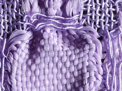 Detailaufnahme eines lilafarbenen Gewebes. Durch zwei unterschiedlich elastische Garne, Gummilitze und Seide, tritt das Blasenmuster des Stoffes besonders hervor. 