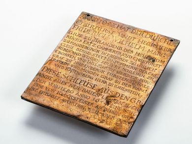 The copper plaque is about the size and weight of a small tablet computer. An early New High German text engraved on the ruffled and furrowed surface provides details about the construction of the Berlin lock in 1657.