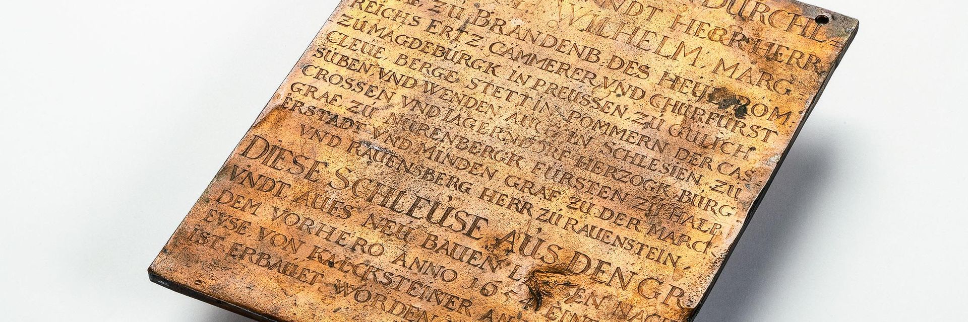 Die Tafel aus Kupfer hat etwa die Maße und das Gewicht eines kleinen Tabletcomputers. In der gewellten und mit Furchen überzogenen Oberfläche ist ein Text eingraviert, der in frühem Neuhochdeutsch vom Bau der Berliner Schleuse im Jahr 1657 berichtet.