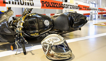 Ein schwarzes Motorrad liegt auf dem Boden, im Vordergrund ist ein Helm zu sehen.
