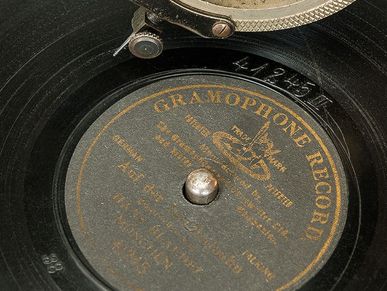 A record lies on green felt. A gramophone arm with a decorated sound box is positioned above it.