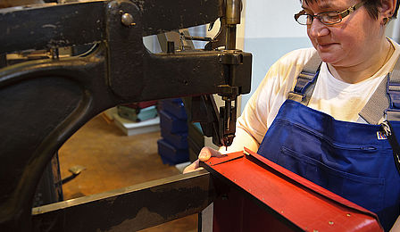 Eine Frau hält eine der Ecken eines roten Unterkoffers unter eine Nietmaschine.