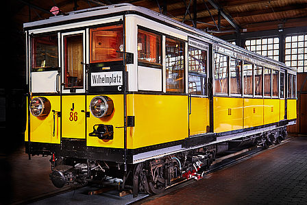Ein historischer U-Bahnwagen steht auf einem Gleis in einem Lokschuppen. Der Wagen ist gelb-weiß gestrichen, die Form ist eckig.