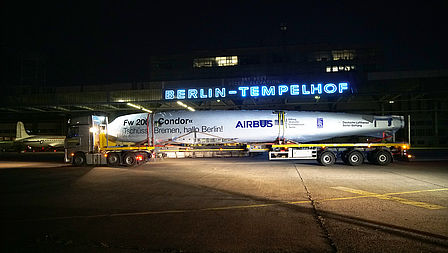 Schwerlasttransporter mit dem Rumpf der Condor steht vor dem Gebäude des Tempelhofer Flughafens.