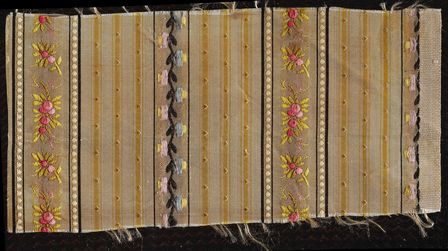 Ein beiger, mit bunten Blumenranken, Streifen und Punkten gemusterte Stoff aus Seide.