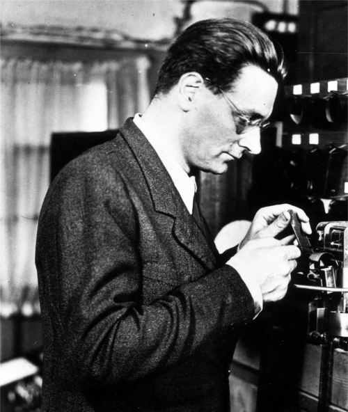 Black-and-white photograph: profile view of Konrad Zuse checking a punch tape.