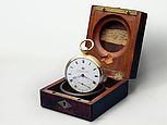 Der Humboldt-Chronometer ist eine Taschenuhr mit weißem Zifferblatt. Die Uhr wird stehend in ihrer Holzschatulle gezeigt.