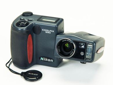 This digital camera consists of two parts, the screen and controls unit and the lens unit. The control unit has a handgrip for holding the camera. The shutter button, two function keys, a setting dial and a small digital display are located on its top face. The lens unit is connected to the control unit with a swivel hinge. It consists of the lens, the viewfinder, a light sensor and a small built-in flash.