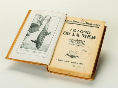 Auf der Titelseite eines aufgeschlagenen Buches sind mittig unter der Überschrift „Le fond de la mer“, französisch für „Der Meeresboden“ Abdrücke von zwei Bibliotheksstempeln zu erkennen.
