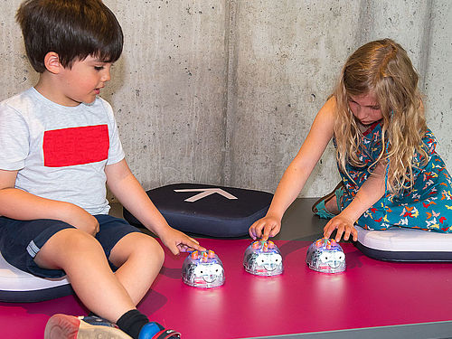 Zwei Kinder lernen in den farbenfrohen Räumen des kids.sigilab mithilfe von Robotikspielzeug zu denken und zu spielen wie ein Computer.