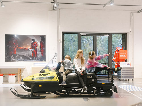Drei Kinder sitzen auf einem Schneemobil in der Sonderausstellung "Dünnes Eis" im Deutschen Technikmuseum.