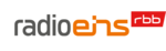 Das Logo des Senders radio eins. Der Schriftzug "radio" in Grau, "eins" in Orange und daneben hochgestellt "rbb" in Weiß auf rotem Grund.