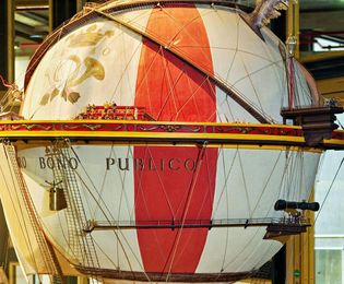 A model of a large, red-and-white-striped hot air balloon. A ship with a city built on its deck hangs from the balloon.