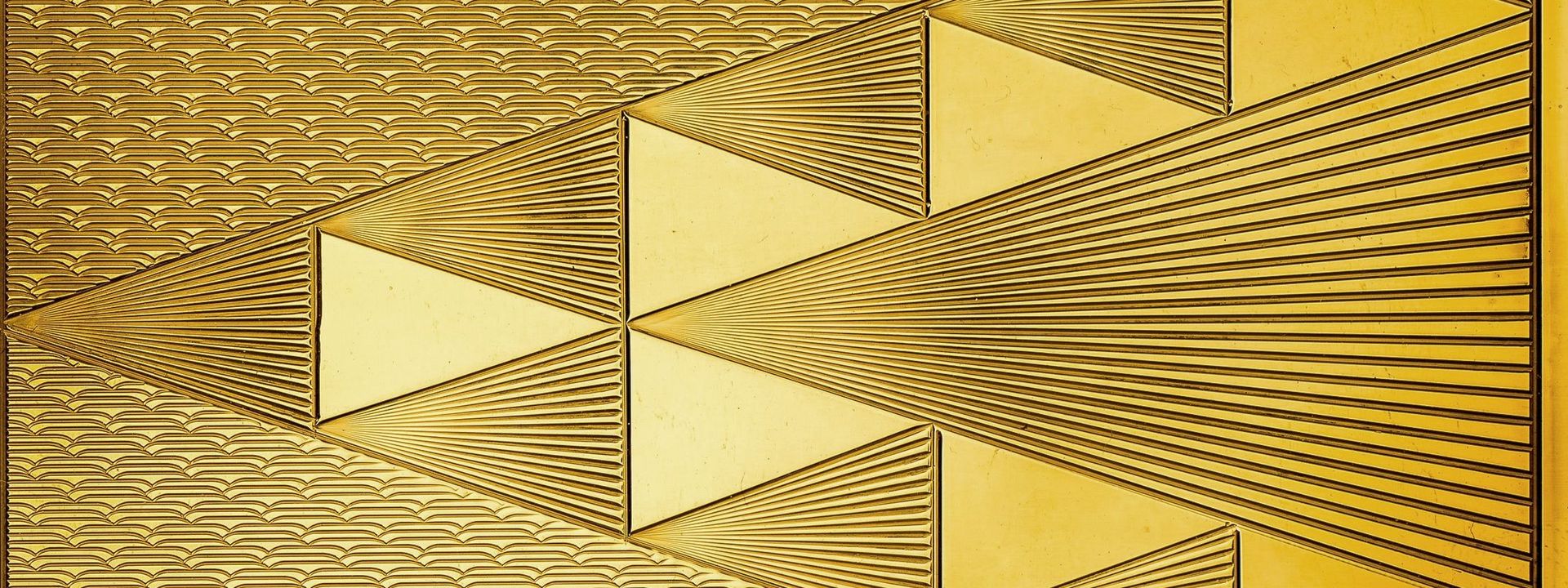 Close-up of a piece of shiny golden metal with geometric pattern engraving.