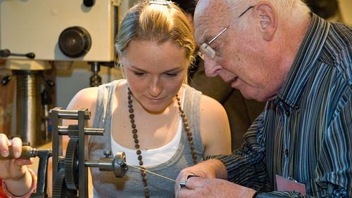 A young woman and an older man work together at a historical machine.