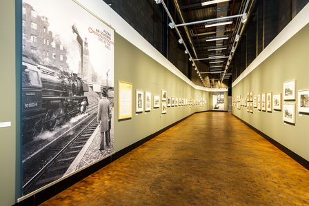 An beiden Seiten des langen Gangs der großen Gallerie hängen Schwarz-Weiß-Fotos an den grau-grünen Wänden. 