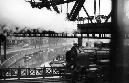 Ein Schwarzweiß-Foto zeigt einen Kanal, über den eine Eisenbahnbrücke führt, außerdem sieht man S-Bahnschienen und eine Straße.