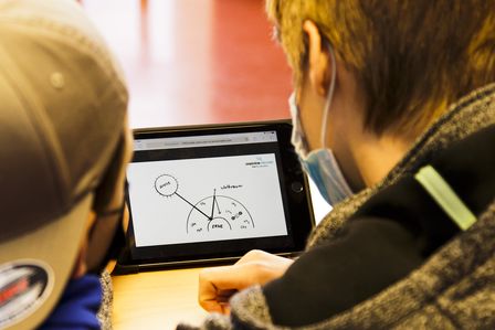 Zwei Jungen schauen auf ein Tablet, auf dem eine grafische Auswertung von Messergebnissen zu sehen ist.
