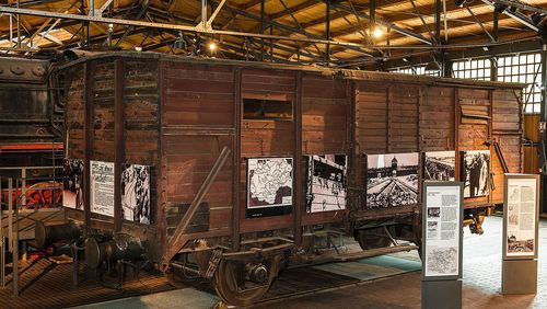 View of an old, brown wooden boxcar. Black-and-white photographs of concentration camps are displayed on the boxcar’s sides. 
