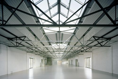 Blick in eine Lagerhalle, die offensichtlich neu restauriert wurde: Die Böden und Wände glänzen weiß, die Stahlkonstruktion der Decken geben den Blick auf Glasgauben frei.