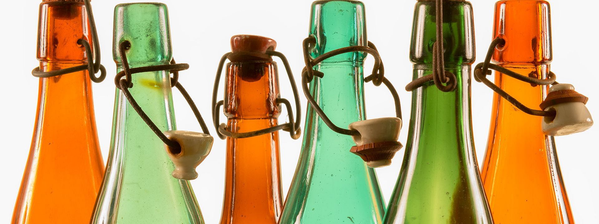 Die Flaschenhälse der historischen Bierflaschen aus braunem und grünem Glas glänzen im Gegenlicht. Ihre Bügelverschlüsse sind teilweise geöffnet.