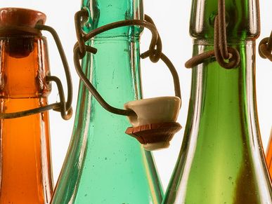 Die Flaschenhälse der historischen Bierflaschen aus braunem und grünem Glas glänzen im Gegenlicht. Ihre Bügelverschlüsse sind teilweise geöffnet.