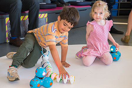 Zwei Kinder spielen mit kleinen blauen Robotern.