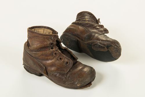 The image shows small, very worn brown leather boots. The laces are missing and holes can be seen in the toe caps and soles.