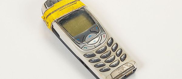 Foto eines alten und abgenutzten Nokia-Handys. Oben hält ein gelbes Tape die beiden Gehäuseschalen zusammen.