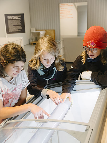 Drei Kinder untersuchen einen zylinderförmigen Eisbohrkern in einer Ausstellungshalle.