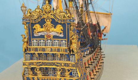 Die Hinteransicht des Modell eines barocken Schiffes vor blauem Hintergrund. Gut sind die kunstvollen Verziehrungen seiner Heckfassade zu sehen.
