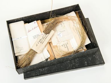 An open gray box with many envelopes and samples of various grass papers as well as dried grasses.