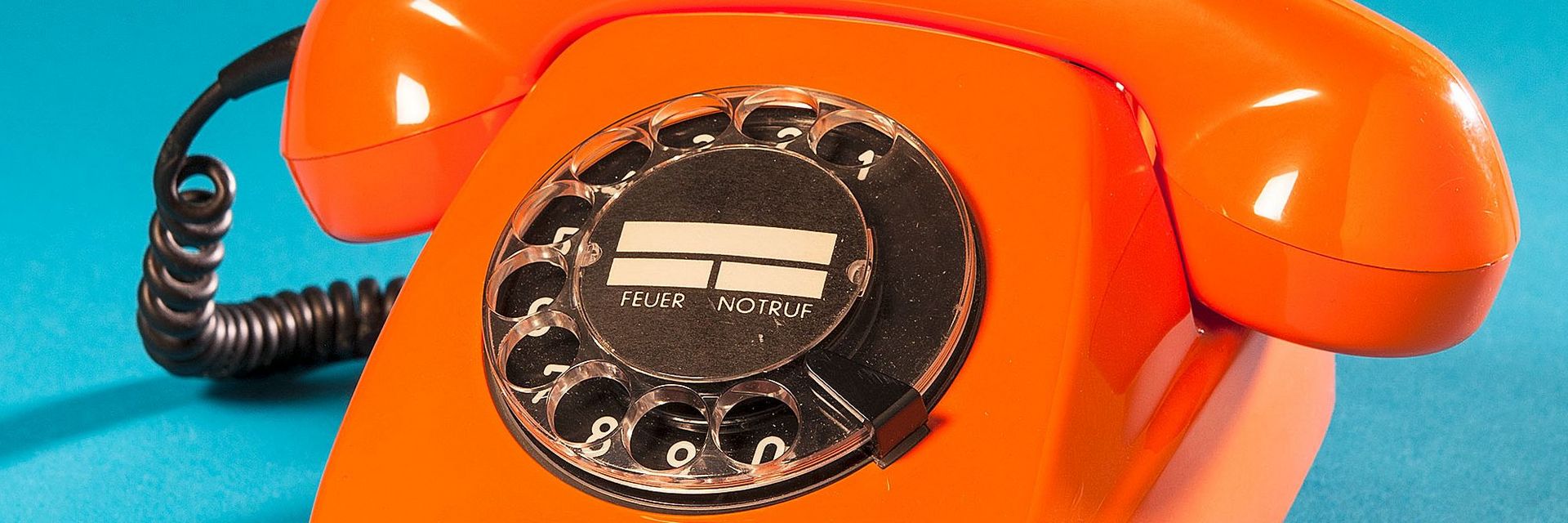 Orangenes, schnurgebundenes Telefon mit schwarzer Wählscheibe.