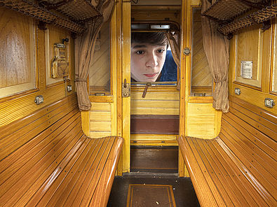 Ein kleiner Junge schaut durch ein Fenster in ein Modell eines Eisenbahnwaggons.