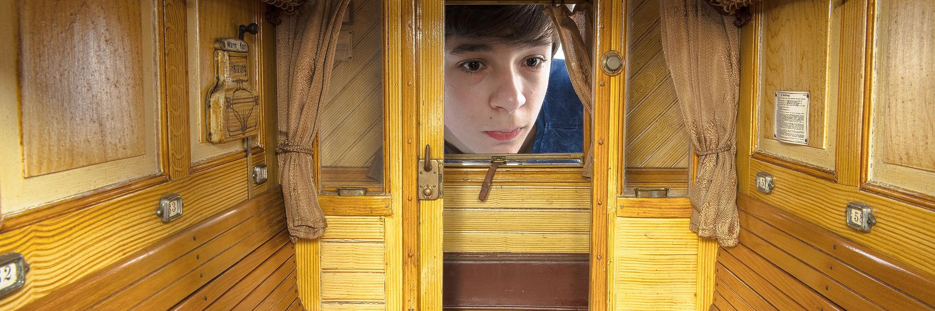 Ein kleiner Junge schaut durch ein Fenster in ein Modell eines Eisenbahnwaggons.
