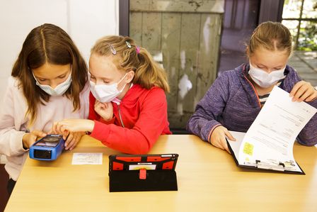 Drei Mädchen sitzen an einem Schreibtisch und schauen konzentriert auf Messgeräte und einen Auswertungsbogen.