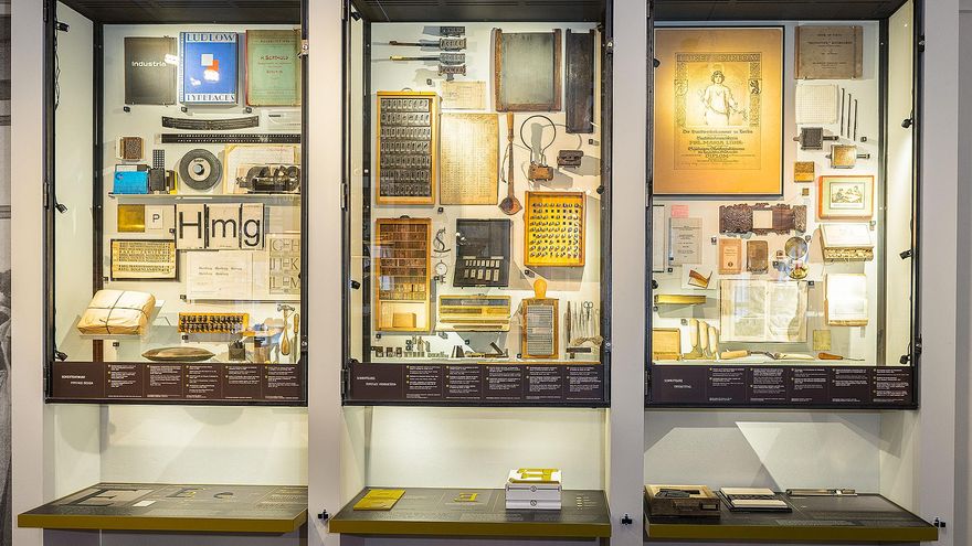 Three wall display cases exhibit many different objects, including books, tools, and matrices.