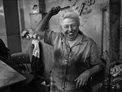 Auf dem Foto ist eine Frau im kohleverschmierten Arbeitskittel zu sehen, die sich lachend die Haare kämmt.